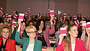 Frauen sitzen in einem großen Konferenzraum und halten Abstimmungskarten in die Luft