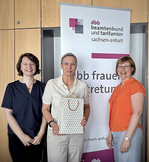 Zwei Frauen überreichen einer dritten Frau eine Geschenktüte