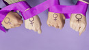 Vier Frauenhände mit einem aufgemalten Frauen-Symbol, ein violettes Band ist um die Handgelenke gelegt