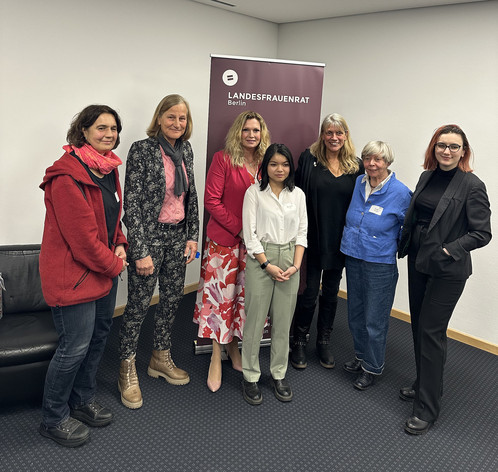 Eine Gruppe Frauen steht vor einem lilanen Roll-Up