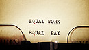 Auf einem in eine Schreibmaschine eingespannten Blatt stehen die getippten Worte "Equal Work - Equal Pay"