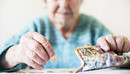 Eine unglücklich wirkende Seniorin zählt am Tisch die wenigen Münzen ihre Pension.