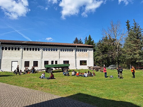 Eine Gruppe Frauen sitzt auf einer Wiese hinter einem Bauernhof.