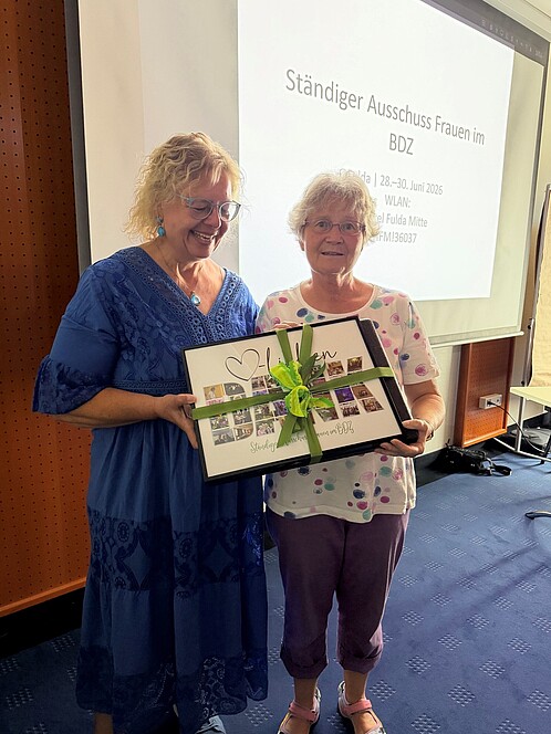 Auf einer Bühne überreicht eine Frau einer anderen ein Geschenk.