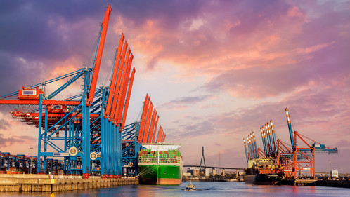 Scenic front giant cargo container ship loading Hamburg city port harbour seaport cranes warm dramatic sky evening sunset light. Global commercial trade freight charter shipping logistics background.