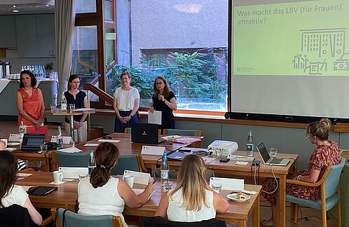 Vier Frauen stehen vorne in einem gut gefüllten Konferenzraum und halten einen Vortrag