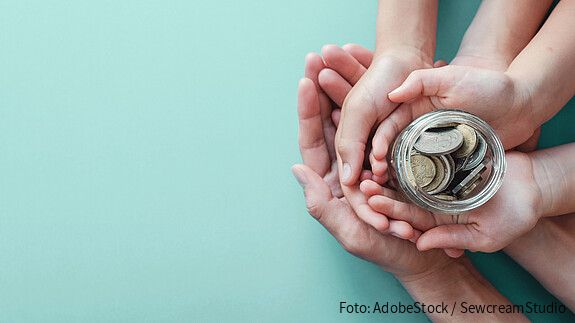 Ein Kind und Erwachsene halten ein Glas mit Geld