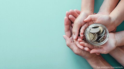 Ein Kind und Erwachsene halten ein Glas mit Geld