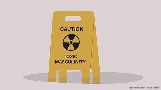 A yellow floor sign warning about toxic masculinity, the idea of manliness as being defined by domination, homophobia, and aggression