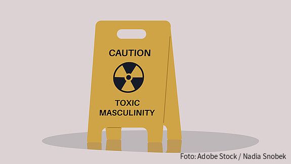 A yellow floor sign warning about toxic masculinity, the idea of manliness as being defined by domination, homophobia, and aggression