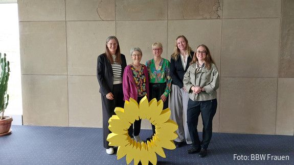 Gespräch der BBW Frauen mit MdL Stefanie Seemann  Fünf Frauen stehen hinter einem gelben Aufsteller im Design einer großen gelben Blüte