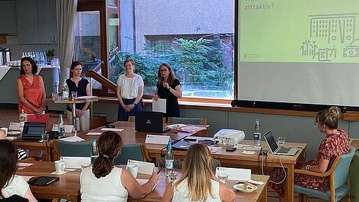 Vier Frauen stehen vorne in einem gut gefüllten Konferenzraum und halten einen Vortrag