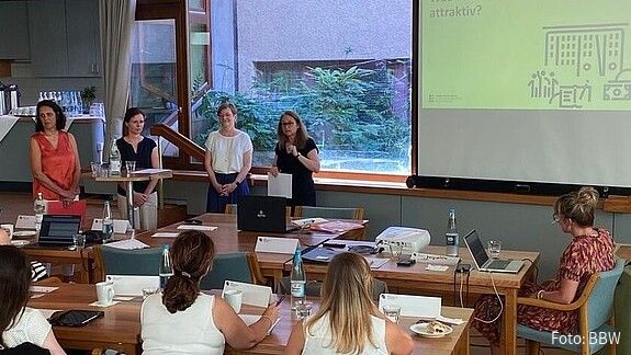Vier Frauen stehen vorne in einem gut gefüllten Konferenzraum und halten einen Vortrag