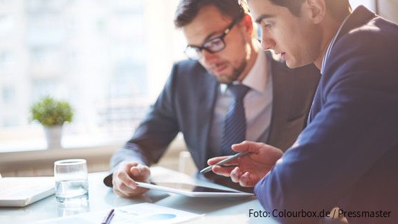 Zwei Männer im Büro sehen gemeinsam auf Tablet und besprechen sich