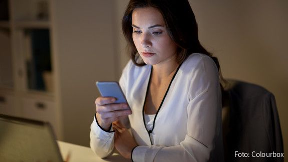 Eine junge Frau im Büro sieht mit ernstem Gesichtsausdruck auf das Display ihres Handys. 