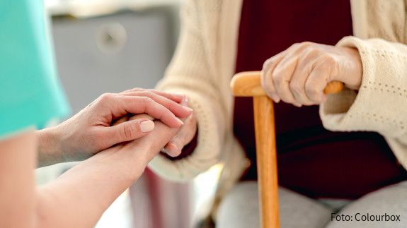 Das Foto zeigt die Hände einer Pflegerin, die die Hände einer Seniorin mit einem Stock halten. Es handelt sich um eine Nahaufnahme.