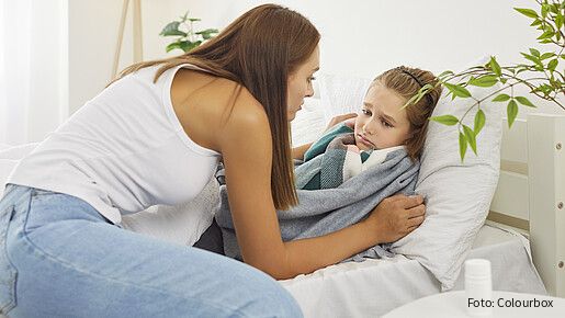 Eine Frau sitzt auf einem Bett und versorgt ihre kranke Tochter