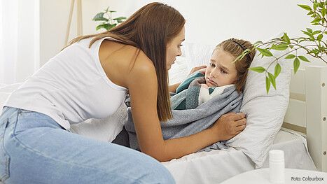 Eine Frau sitzt auf einem Bett und versorgt ihre kranke Tochter