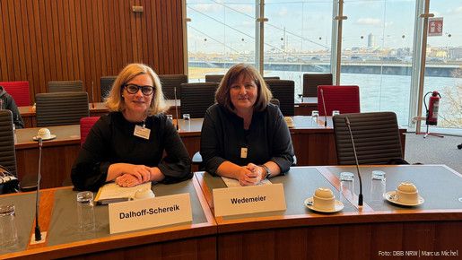 Zwei Frauen sitzen an einem Tisch in einem Plenarsaal