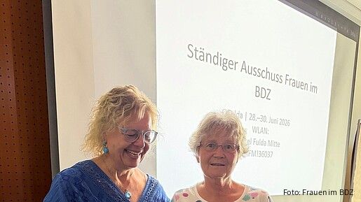 Auf einer Bühne überreicht eine Frau einer anderen ein Geschenk.