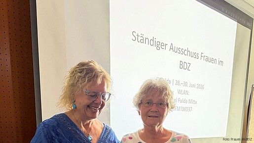 Auf einer Bühne überreicht eine Frau einer anderen ein Geschenk.