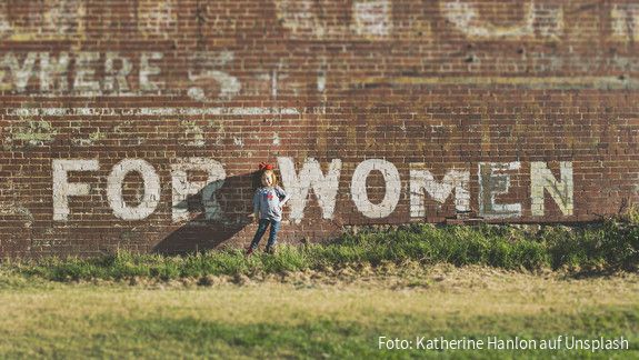 Ein Mädchen steht vor einer Wand auf der For Women steht