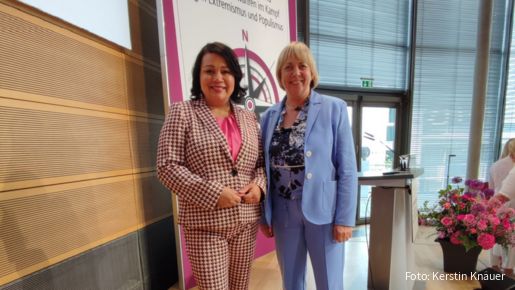 Zwei Frauen stehen auf einer Bühne und schauen in die Kamera