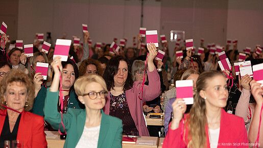 Frauen sitzen in einem großen Konferenzraum und halten Abstimmungskarten in die Luft