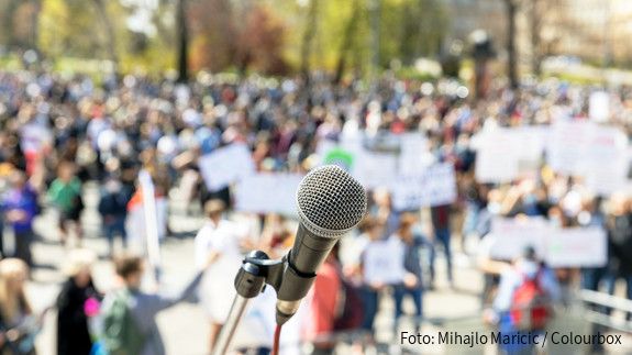 Protest or public demonstration, focus on microphone, blurred group of people in the background protest, demonstration, people, group, crowd, banner, microphone, protester, political, social, democracy, anti-racism, strike, street, movement, politic, rally, audience, speaker, public, auditorium, mass, event, right, human, orator, civil, unrecognizable, activism, justice, election, meeting, labor, nonviolent, convention, resistance, climate, covid-19, lockdown, coronavirus, pandemic, resist, politics, protesters, rights, recording, presentation, demonstrations