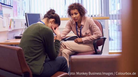 Psychische Belastung im Dienst: Gesundheitsprävention umfasst mehr als einen ergonomischen Arbeitsplatz  Junge Frau im Gespräch mit einer weiblichen Vertrauensperson über psychische Belastungen