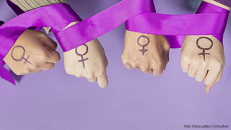 Vier Frauenhände mit einem aufgemalten Frauen-Symbol, ein violettes Band ist um die Handgelenke gelegt
