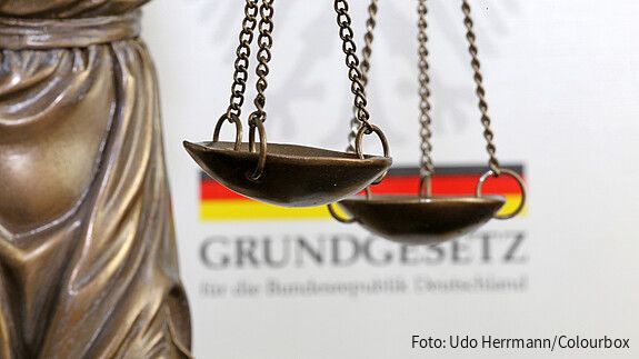 Nahaufnahme einer Justitia vor dem deutschen Grundgesetzbuch