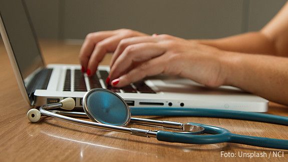 Hände tippen auf Tastatur, davor liegt ein Stethoskop