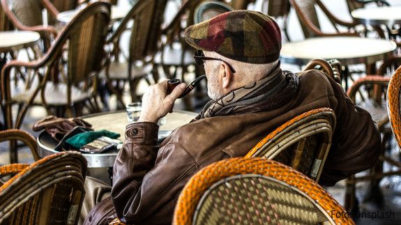 Ein älterer Herr sitzt in einem Café und raucht Pfeife. 