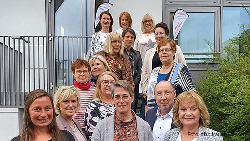 Eine Gruppe Menschen steht auf einer Treppe vor einem Haus und schaut in die Kamera.