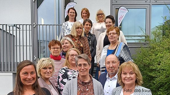 Eine Gruppe Menschen steht auf einer Treppe vor einem Haus und schaut in die Kamera.