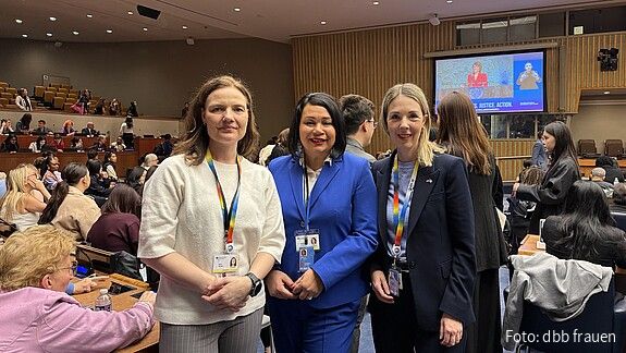 drei Frauen stehen im einem Plenarsaal und blicken in die Kamera.
