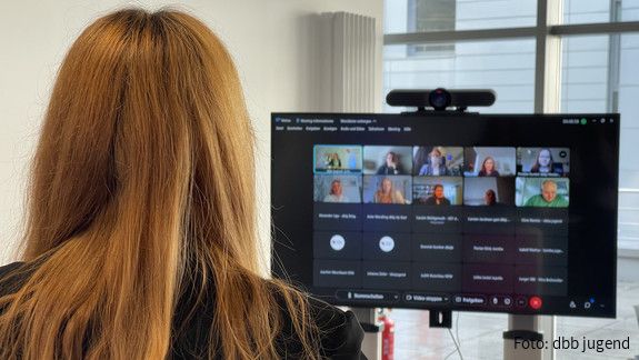 Bundesjugendausschuss Januar 2022 Eine rothaarige Frau sitzt mit dem Rücken zur Kamera und guckt auf einen Bildschirm. Auf dem Bildschirm ist eine Videokonferenz zu sehen.