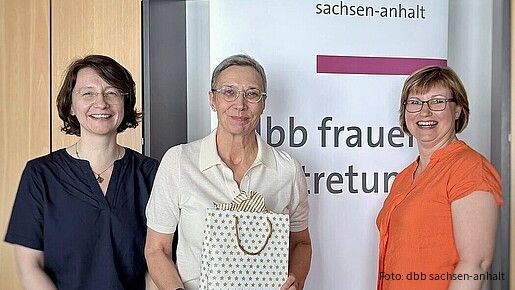 Zwei Frauen überreichen einer dritten Frau eine Geschenktüte