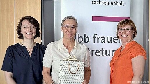 Zwei Frauen überreichen einer dritten Frau eine Geschenktüte