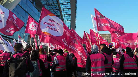 Menschen demonstrieren mit pinken Fahnen auf einem öffentlichen Platz.