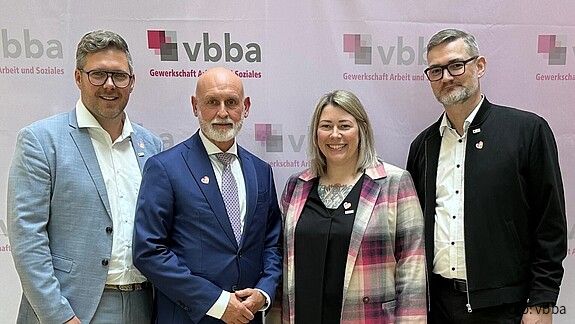 Gruppenfoto von Männern und Frauen vor einem Logo-Aufsteller