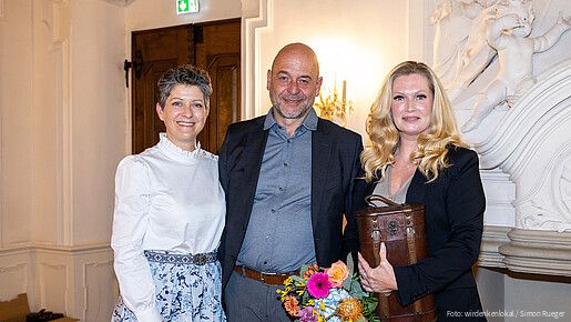 zwei Frauen und ein Mann stehen in einem Konferenzraum und blicken lächelnd in die Kamera